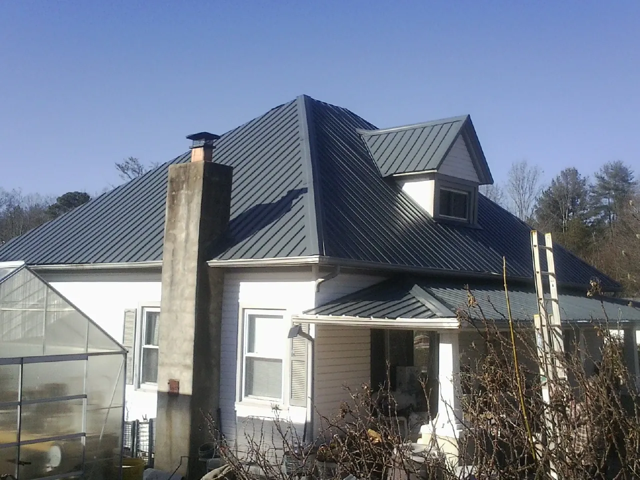 Dark blue standing seam metal roof on a white farmhouse with dormer — Slate & Tile Roof Repair by Roofing Brothers in Ivins