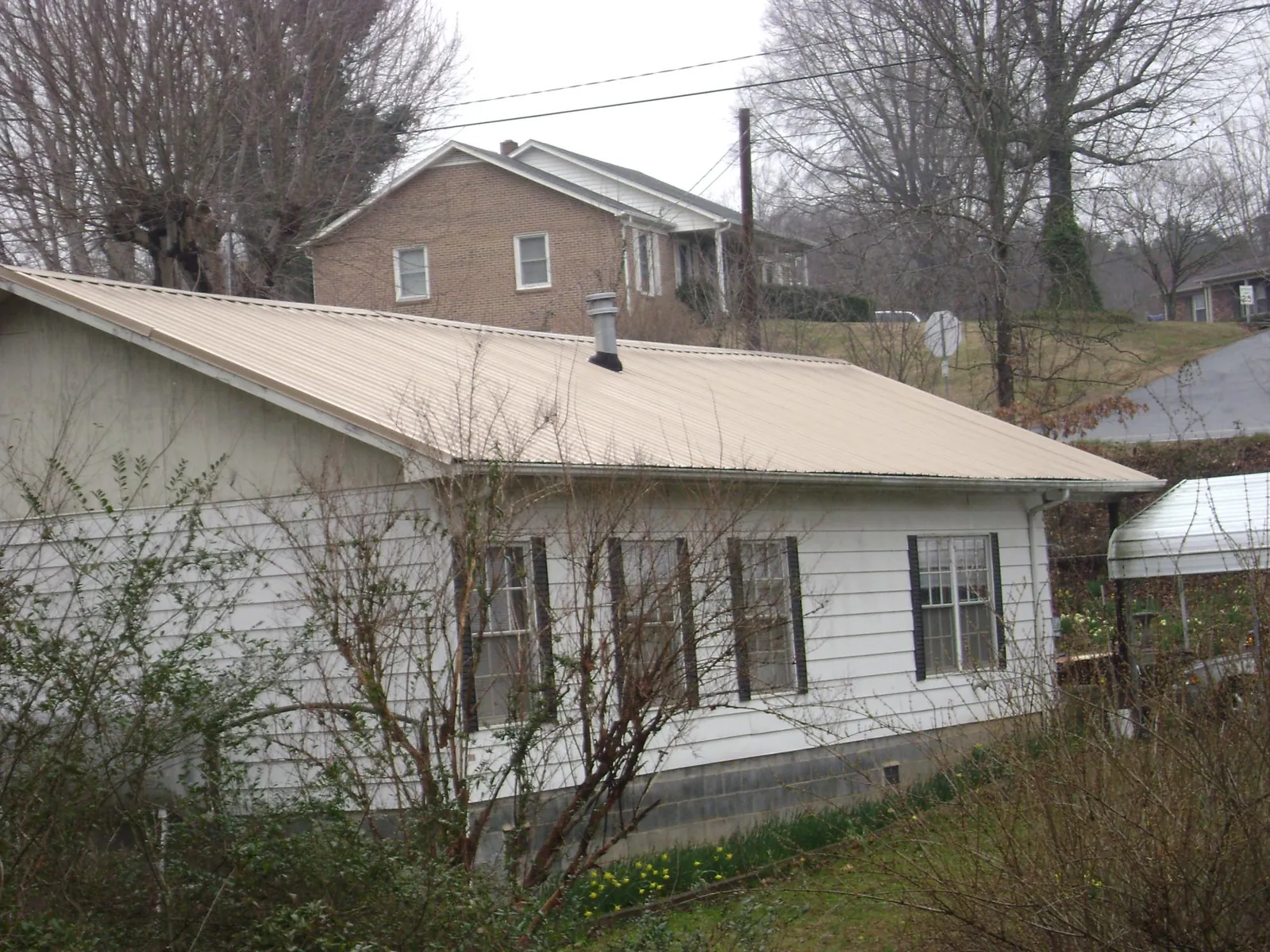 Tan metal roof on a white sided house set into a hillside — Commercial Roofing by Roofing Brothers in Ivins